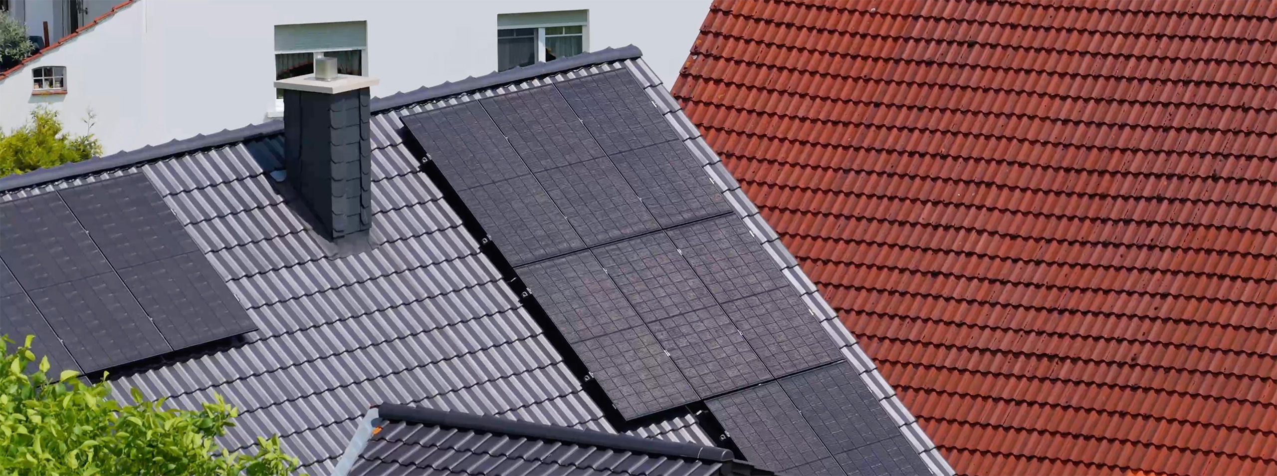 Graues Dach mit mehreren Solarzellen und rotes benachbartes Ziegeldach.