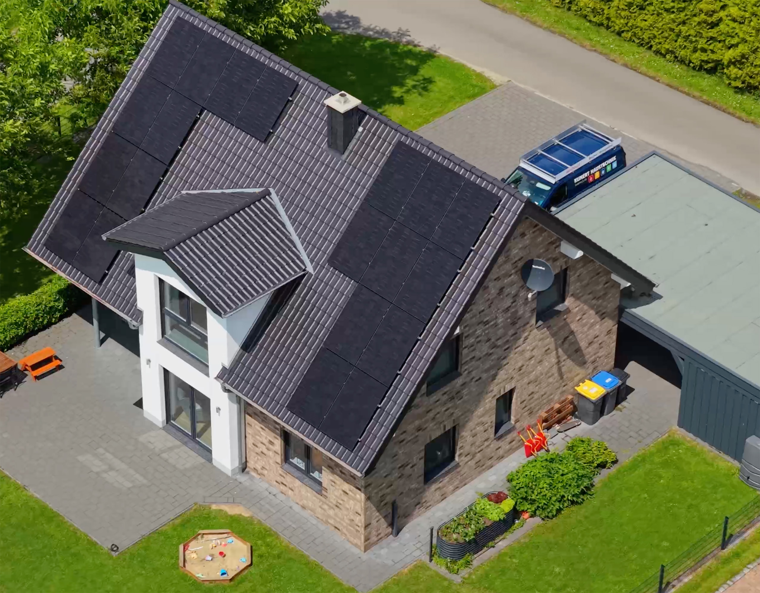 Ein modernes Einfamilienhaus mit Solarpaneelen auf dem Dach und umgeben von grünem Rasen.