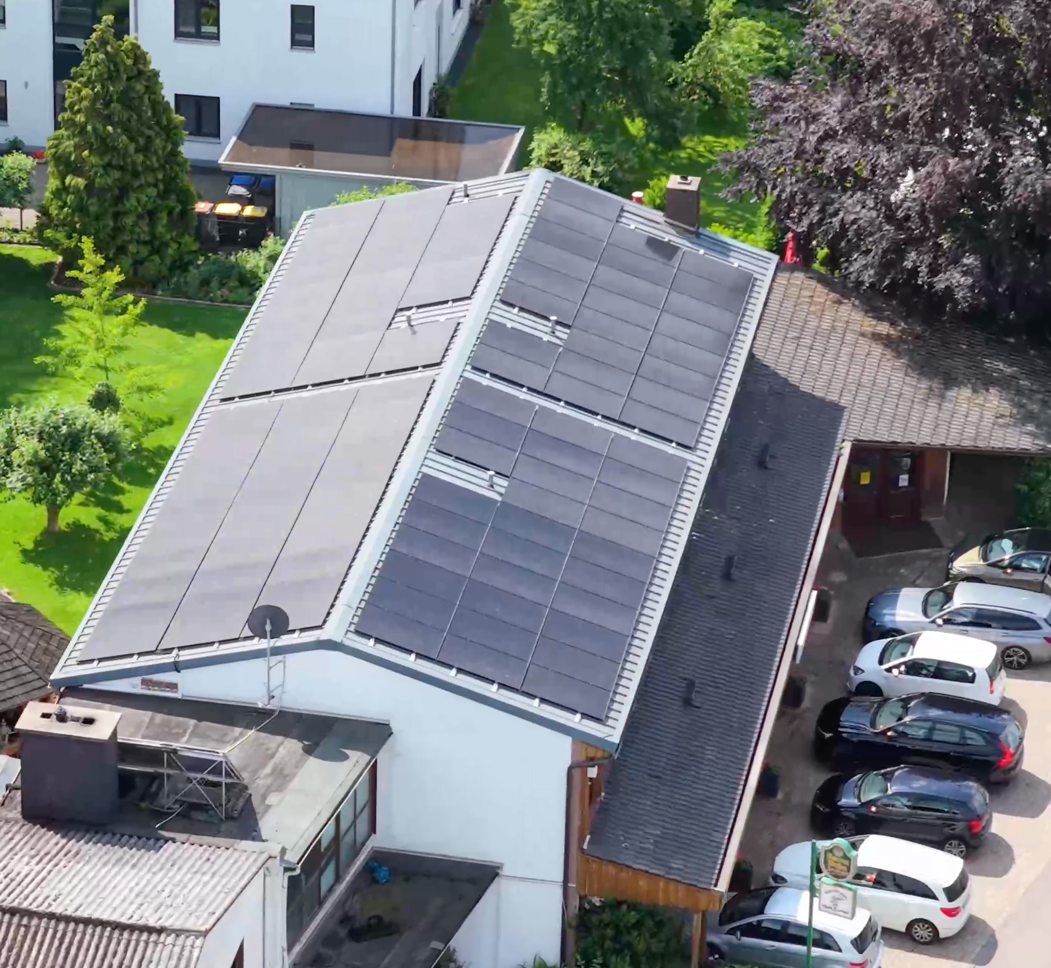 Dach eines Hauses mit Solarmodulen und mehreren parkenden Autos in einer grünen Wohngegend.