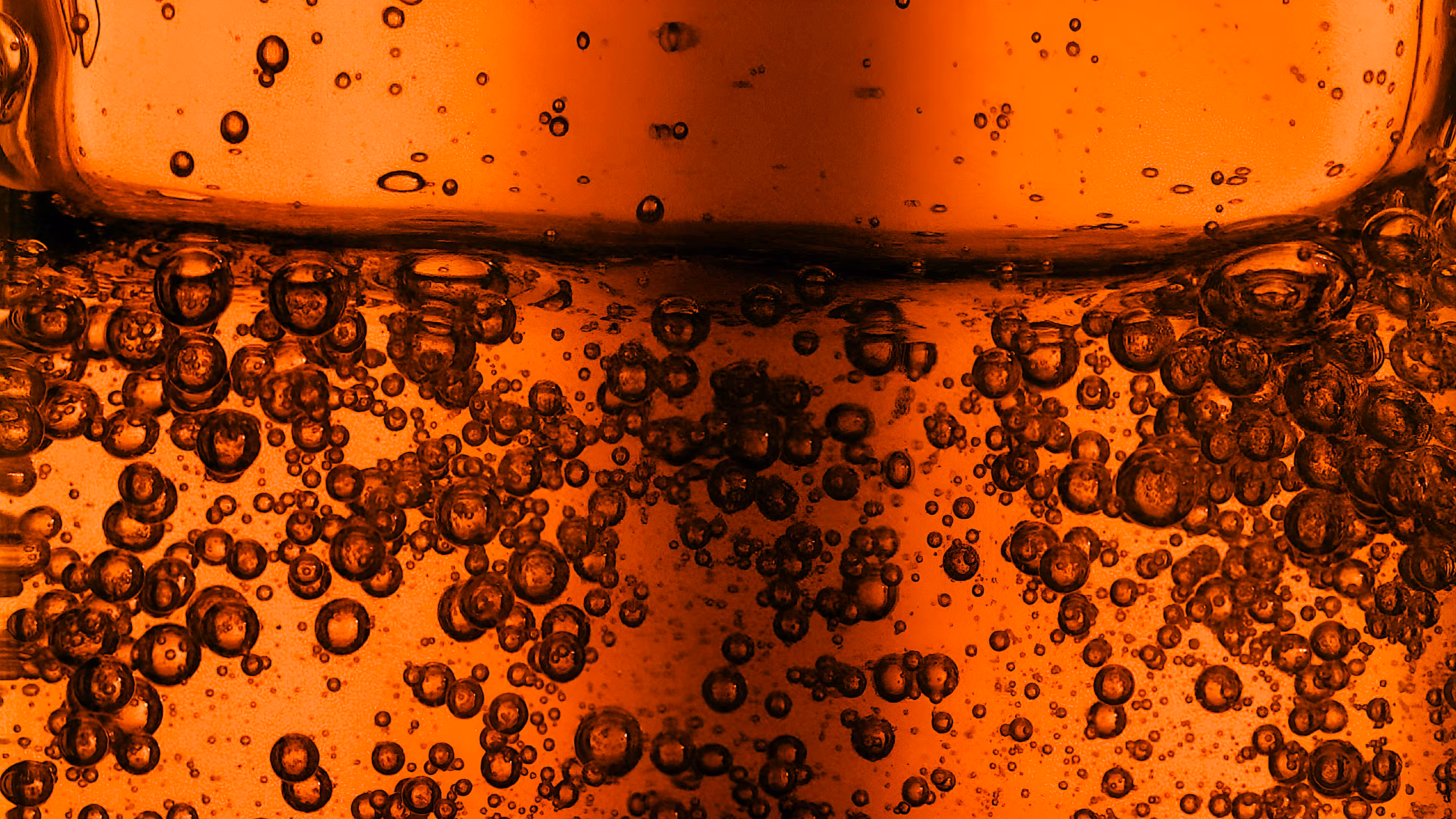 Close-up of numerous bubbles suspended in an orange liquid with a thick layer at the top.