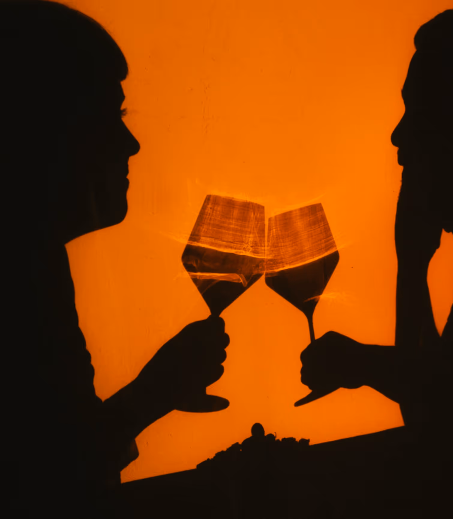 Silhouettes of two people clinking wine glasses against an orange background.