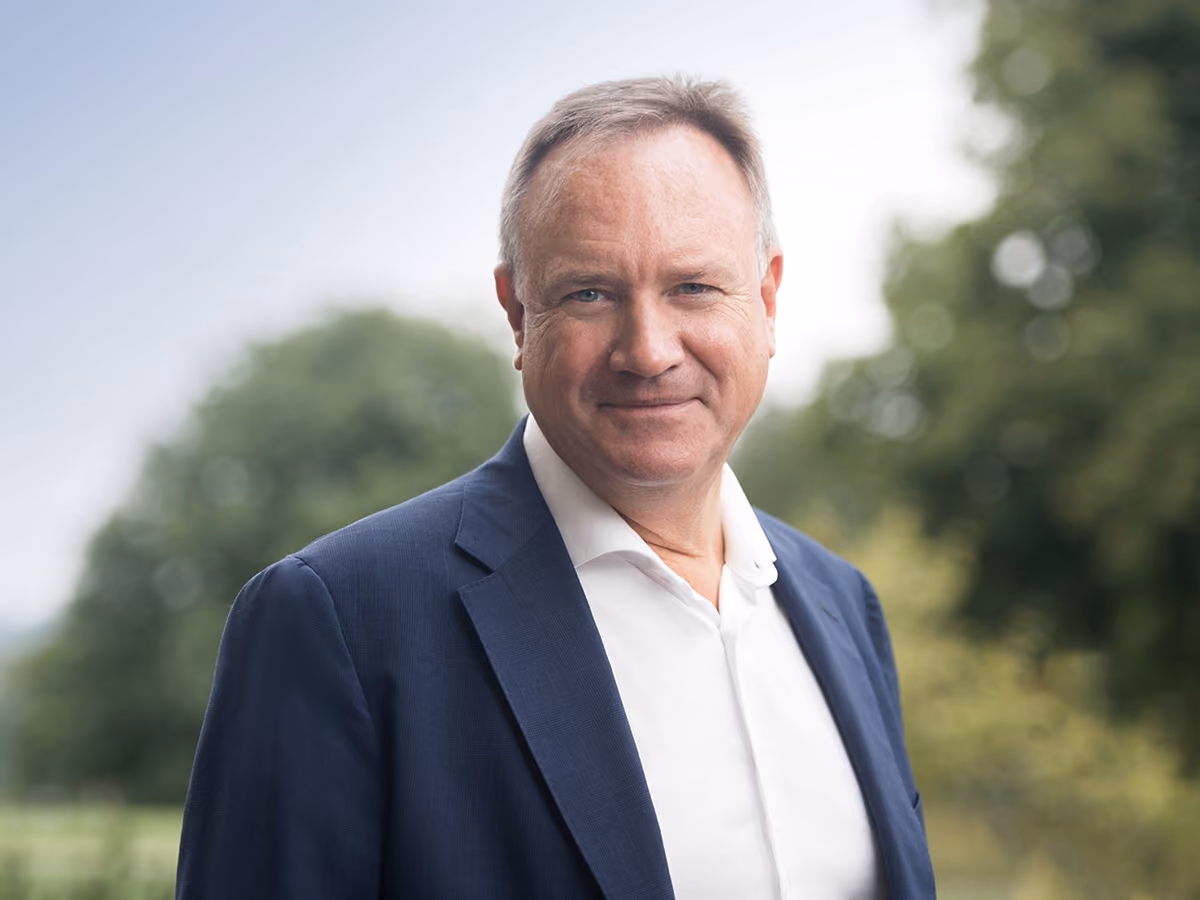 Dr. Markus v. Voss trägt ein dunkelblaues Sakko und ein weißes Hemd, im Freien vor verschwommenem grünem Hintergrund.