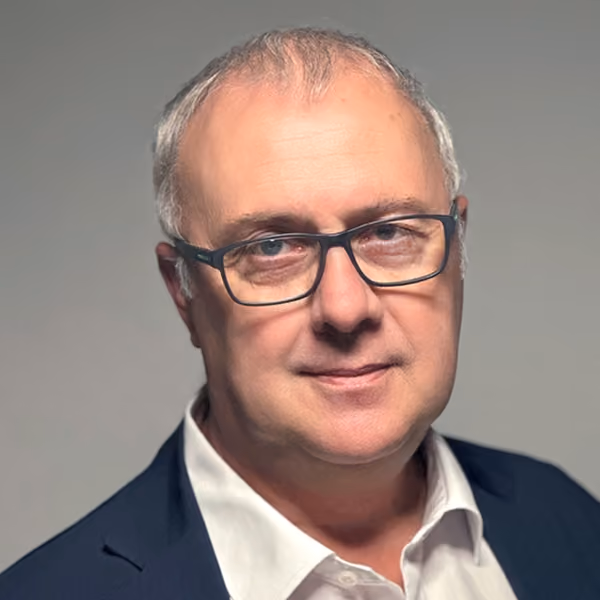Martin Kaczor, der schwarze Brille trägt und einen blauen Anzug mit hellblauem Hemd anhat, vor unscharfem Hintergrund.