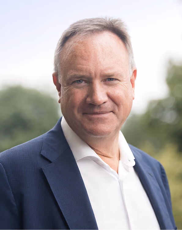 Dr. Markus v. Voss in einem weißen Hemd und dunkelblauem Sakko vor verschwommenem natürlichem Hintergrund.