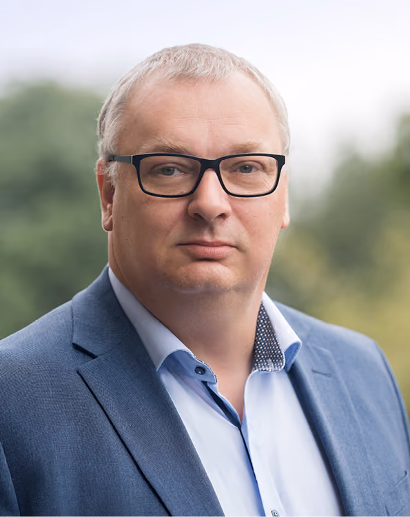 Christian Kuhlmann in blauem Anzug und weißem Hemd vor unscharfem grünem Hintergrund.