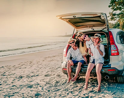 Familie genießt den Sonnenuntergang am Strand und sitzt während ihres Aufenthalts im Mahogany Hôtel Résidence & Spa im Kofferraum ihres Mietwagens.