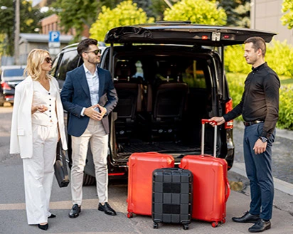 Ankunft im Mahogany Hôtel Résidence & Spa: Ein Gäste-Paar und Hotelmitarbeiter am offenen Kofferraum eines schwarzen Vans.