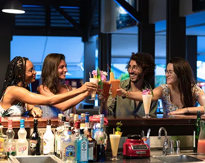 Eine Gruppe von Freunden feiert an der Hotelbar mit Blick auf die Lagune im Mahogany Hôtel Résidence & Spa, Le Gosier, Guadeloupe.
