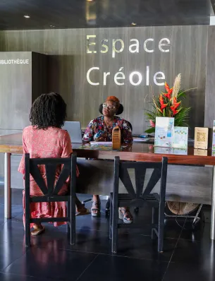 Empfangspersonal begrüßt einen Gast an der Rezeption im Empfangsbereich des Hotels Résidence & Spa Mahogany in Le Gosier, Guadeloupe.