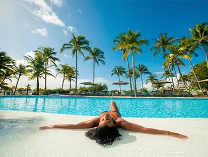 Une femme profitant du soleil au bord de la piscine à débordement du Mahogany Hôtel Résidence & Spa, Pointe de la Verdure, 97190 Le Gosier, Guadeloupe.