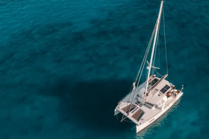 Gros plan aérien d'un catamaran et de son ombre sur l'eau cristalline, près du Mahogany Hôtel, Guadeloupe.