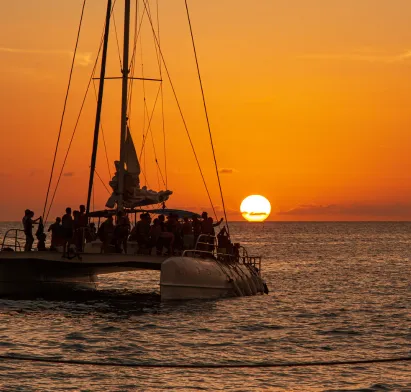 Silhouette eines Katamarans mit Passagieren bei Sonnenuntergang in Guadeloupe, Kreuzfahrt ab dem Hotel Mahogany Résidence & Spa.