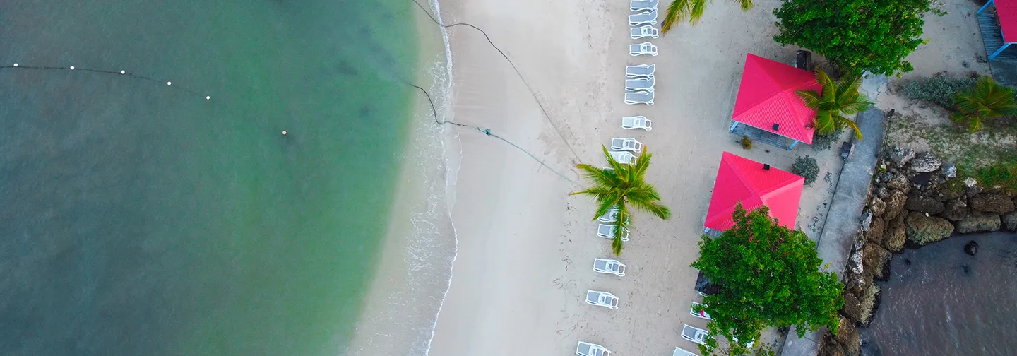 Vista aérea parcial de la playa del Mahogany Hôtel, con sus aguas cristalinas y sombrillas rosas, Le Gosier, Guadalupe.