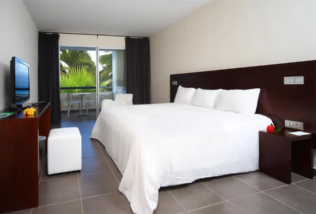 Geräumiges Zimmer mit Sitzecke und Zugang zu einem begrünten Balkon. Mahogany Hôtel Résidence & Spa, Le Gosier, Guadeloupe.