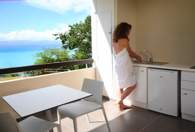 Eine Frau in ein Handtuch gewickelt benutzt das Waschbecken der Kochnische auf dem Balkon. Mahogany Hôtel Résidence & Spa, Le Gosier, Guadeloupe.