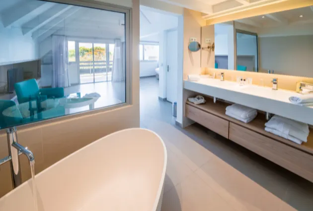 Salle de bain avec baignoire îlot et double vasque, donnant sur une chambre. Mahogany Hôtel, Guadeloupe.