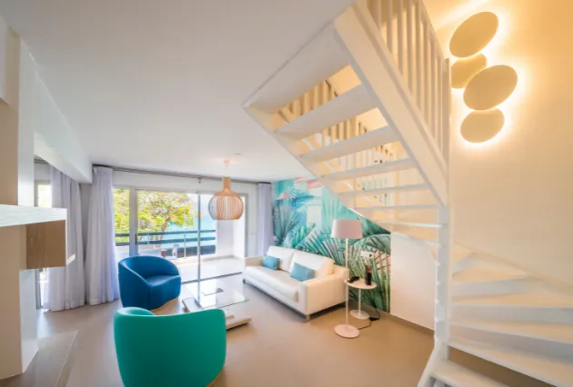 Salon du duplex avec canapé blanc et escalier en colimaçon, vu de l'entrée. Mahogany Hôtel, Guadeloupe.