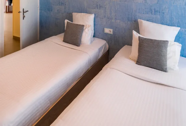 Chambre avec deux lits simples et tête de lit texturée bleue. Mahogany Hôtel, Guadeloupe.