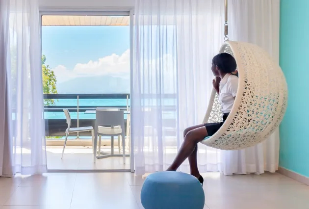 Femme assise dans un fauteuil suspendu en osier, regardant la mer. Mahogany Hôtel, Guadeloupe.