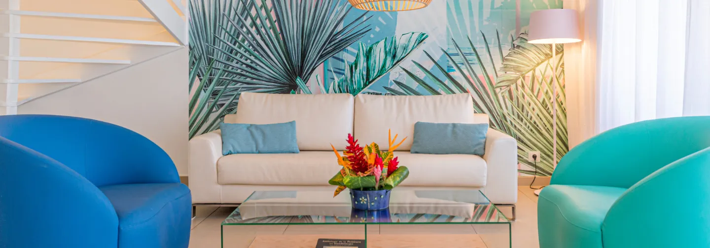 Wohnzimmer der Mahogany Suite mit Sofa, Rattanleuchten und Pflanzenfresko im Hôtel Résidence & Spa Mahogany, Le Gosier, Guadeloupe.
