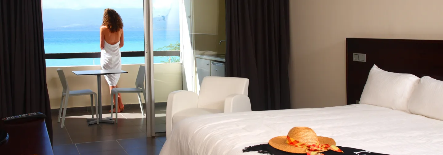 Femme en serviette au balcon, admirant l'océan depuis sa chambre. Mahogany Hôtel Résidence & Spa, Le Gosier, Guadeloupe.