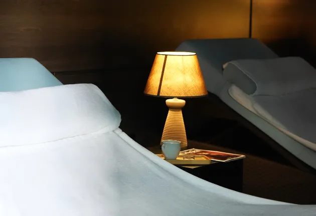 Spa beds with white towels, a lit bedside lamp, and a cup on a table, Mahogany Hôtel Résidence & Spa, Le Gosier, Guadeloupe.