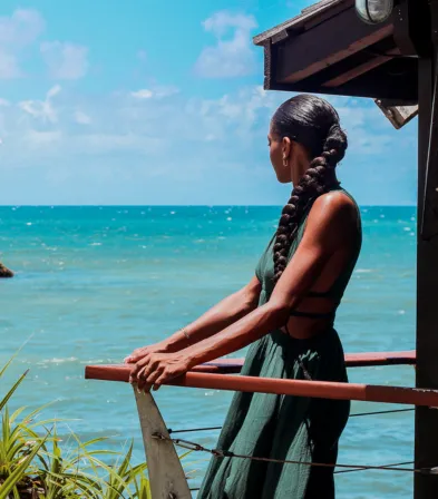 Femme profitant de la vue panoramique sur l'océan depuis son balcon privé au Mahogany Hôtel & Spa, Le Gosier, Guadeloupe.