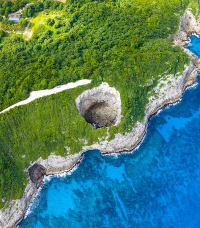 Die felsige Landspitze und das kristallklare Wasser aus der Vogelperspektive im Mahogany Hôtel Résidence & Spa, Guadeloupe.