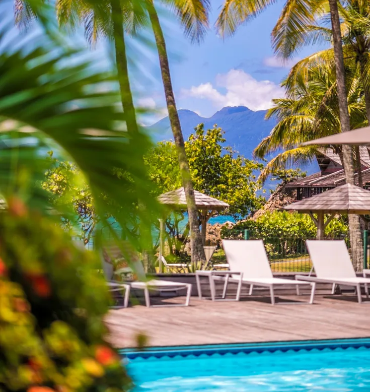 Blick auf den Pool und die Carbets des Mahogany Hotels mit der Soufrière im Hintergrund, Guadeloupe.