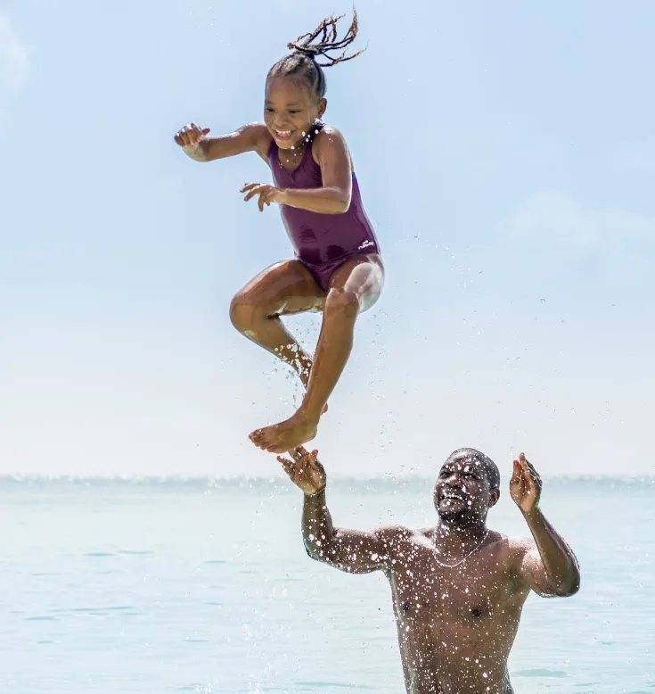 Éclaboussures de joie ! Un père lance sa fille dans les eaux cristallines de la Guadeloupe.