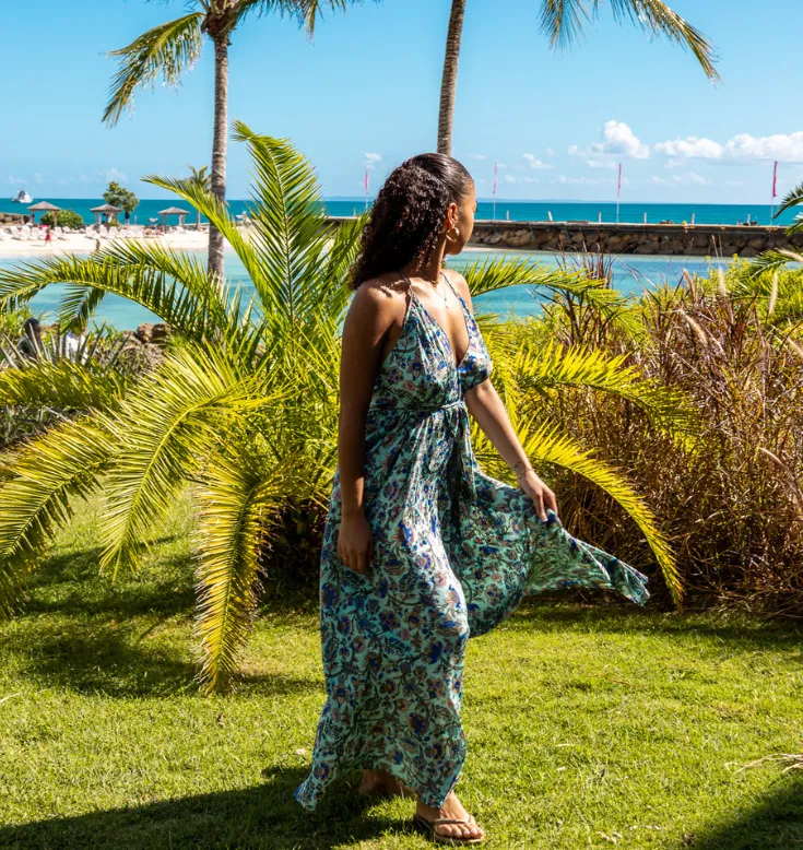 Une femme en robe fleurie marchant dans les jardins luxuriants du Mahogany Hôtel, Guadeloupe.