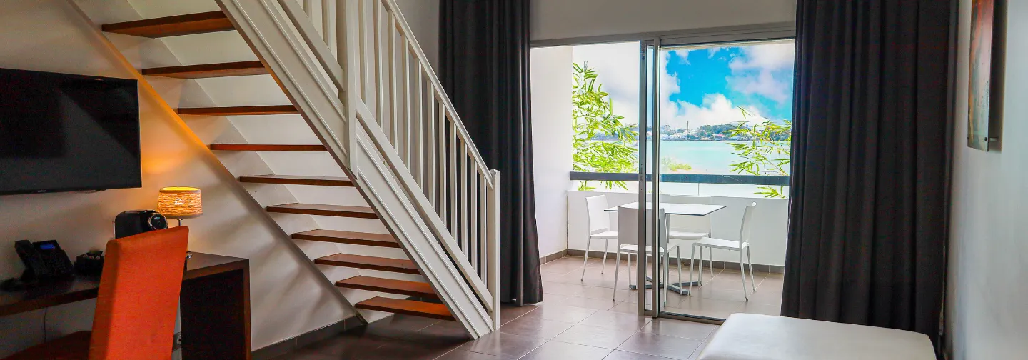 Vista de la terraza amueblada y el mar desde el interior de una suite del Mahogany Hôtel Résidence & Spa.