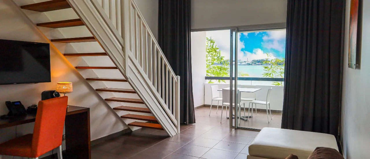 Room with a staircase and desk area, offering a stunning view of the sea. Mahogany Hôtel Résidence & Spa.