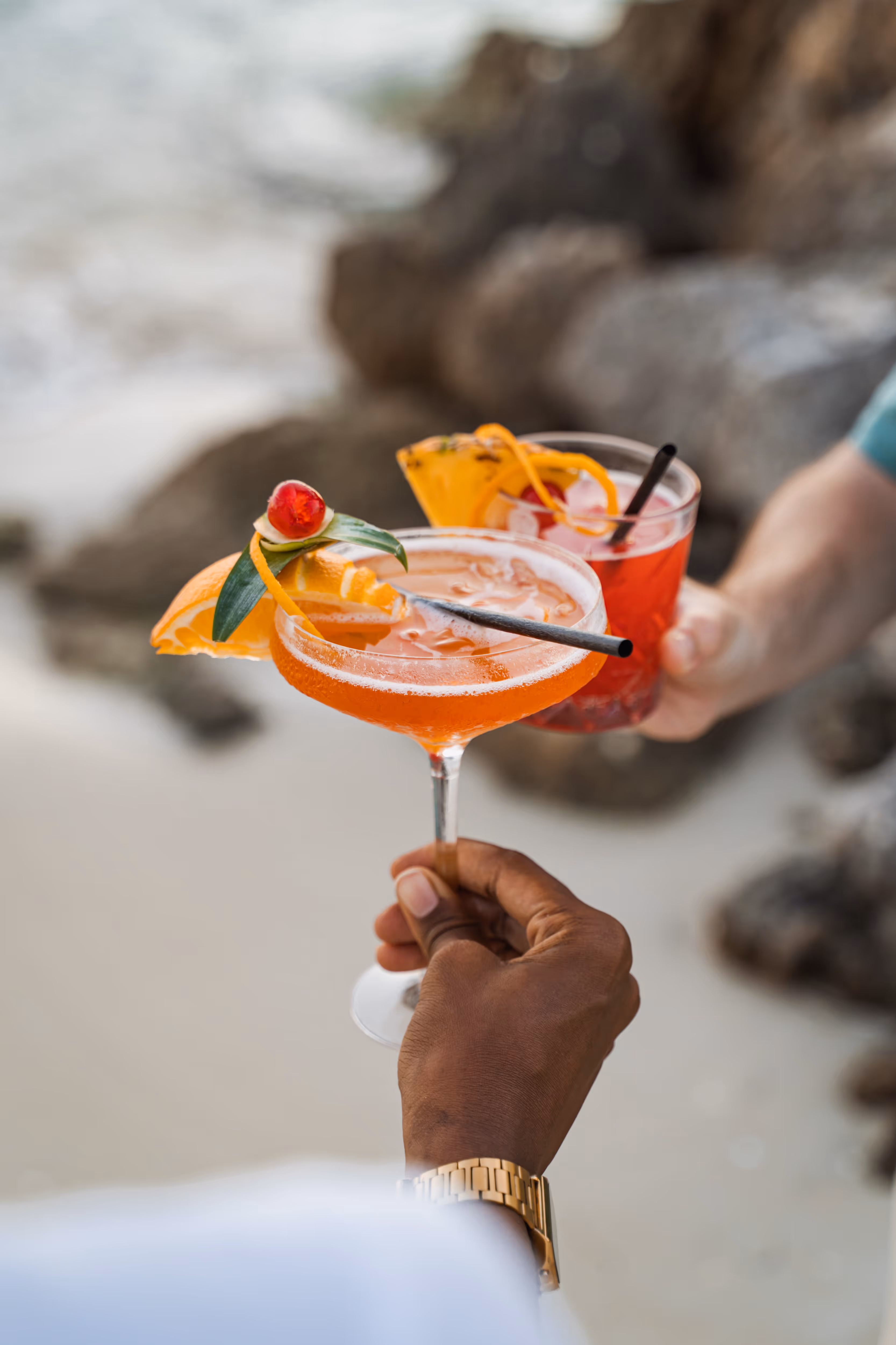 Roter Cocktail mit einer Orangenscheibe auf Felsen am Meer in der Nähe des Hotels Résidence & Spa Mahogany, Le Gosier, Guadeloupe.