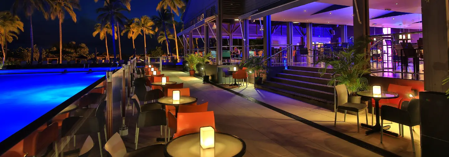 Terrasse de l'hôtel la nuit avec piscine éclairée en bleu et mobilier, Mahogany Hôtel Résidence & Spa, Le Gosier.