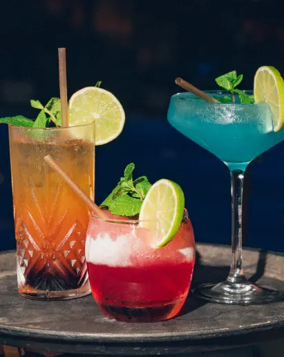 Un cocktail rouge, un bleu et un orange avec garnitures sur une table sombre au Mahogany Hôtel Résidence & Spa, Le Gosier, Guadeloupe.