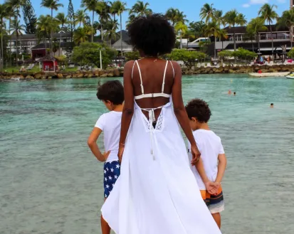 Rückansicht einer Frau und zweier Kinder, die auf eine von Palmen gesäumte Lagune in der Nähe des Mahogany Hotels auf Guadeloupe zugehen.