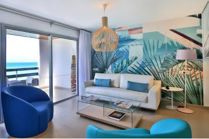 Heller Innenbereich des Mahogany Hôtel Résidence & Spa in Guadeloupe, der die mit Blättern bedruckte Wand und die farbenfrohen Möbel hervorhebt.