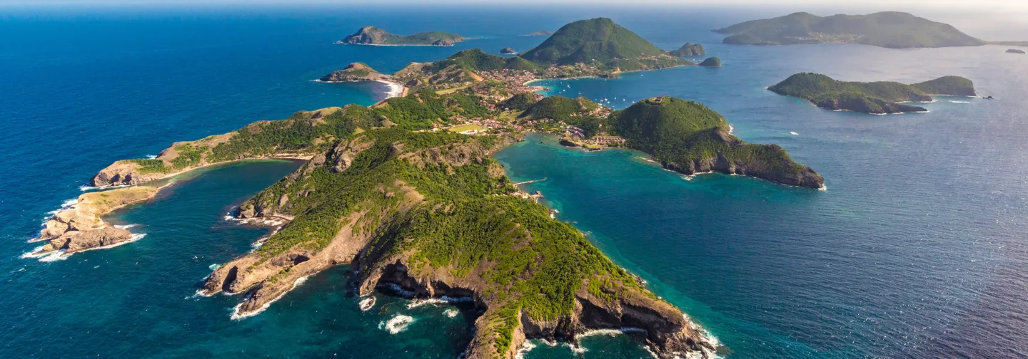 Vue aérienne panoramique de l'archipel des Saintes en Guadeloupe, avec ses collines verdoyantes, ses baies et villages, non loin de l'Hôtel Résidence & Spa Mahogany.