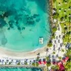 Una vista aérea directa sobre la bahía en forma de herradura, que muestra el contraste entre la arena blanca y los bancos de color turquesa intenso, con un pontón de madera a la izquierda. Mahogany Hotel Residence & Spa, Pointe de la Verture, 97190 Le Gosier, Guadalupe.