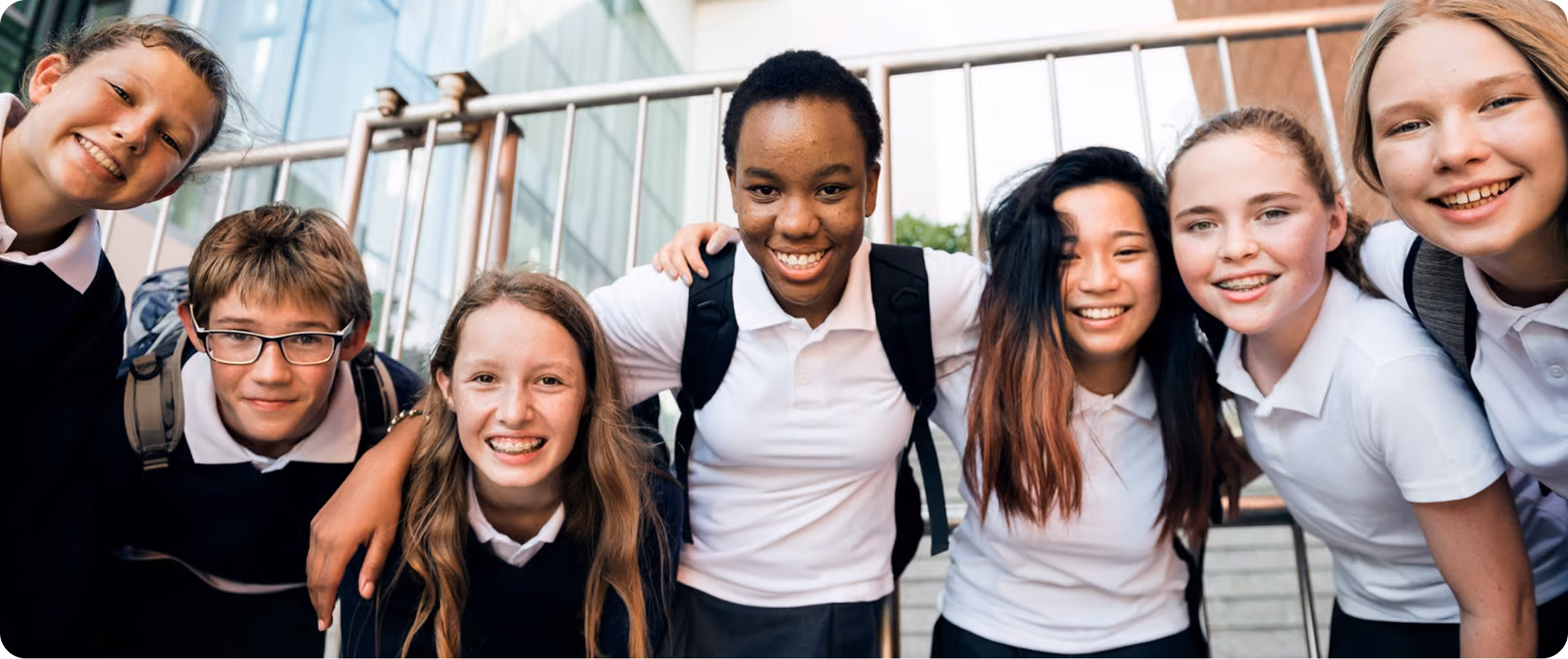 Group of smiling diverse teenagers in school uniforms posing closely outdoors.