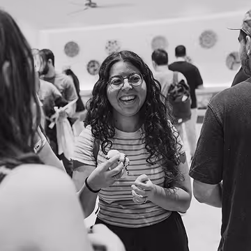 Smiling woman with glasses and curly hair talking with people in a social gathering.