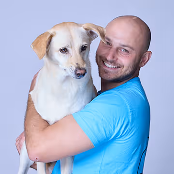 Smiling man in blue shirt holding a white dog.