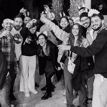 Group of friends smiling and raising drinks, enjoying a lively outdoor celebration at night.
