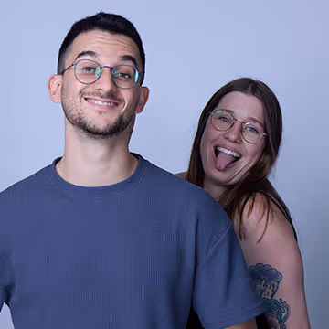 Smiling man in glasses and woman behind him, both wearing glasses.