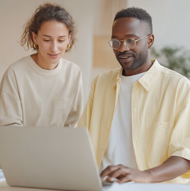 A woman and man looking at a laptop screen together while seated indoors.