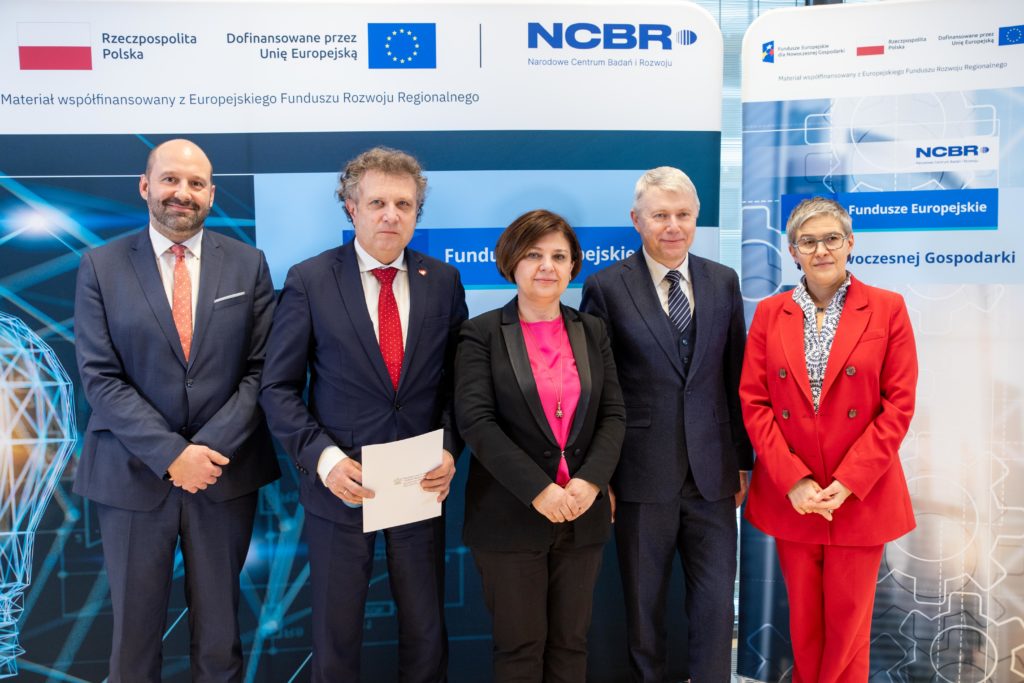 Five officials stand before NCBR and European Funds banners at the STEP project agreement event