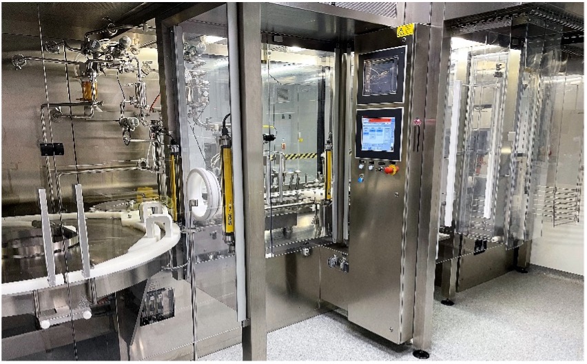 Stainless steel vial filling and capping station with glass enclosure and touchscreen controls in a cleanroom