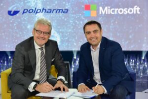 Two men signing documents at a table beneath Polpharma and Microsoft logos