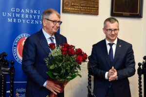 Jerzy Starak holding a bouquet of red roses beside a man in a suit at the Medical University of Gdansk